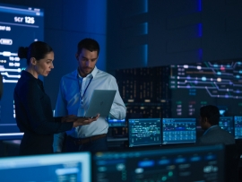 2 people discuss data on a laptop with a screen showing charts and system analysis.